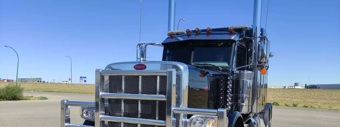 Black Peterbilt highway tractor with polished chrome grille guard and stacks under a blue sky